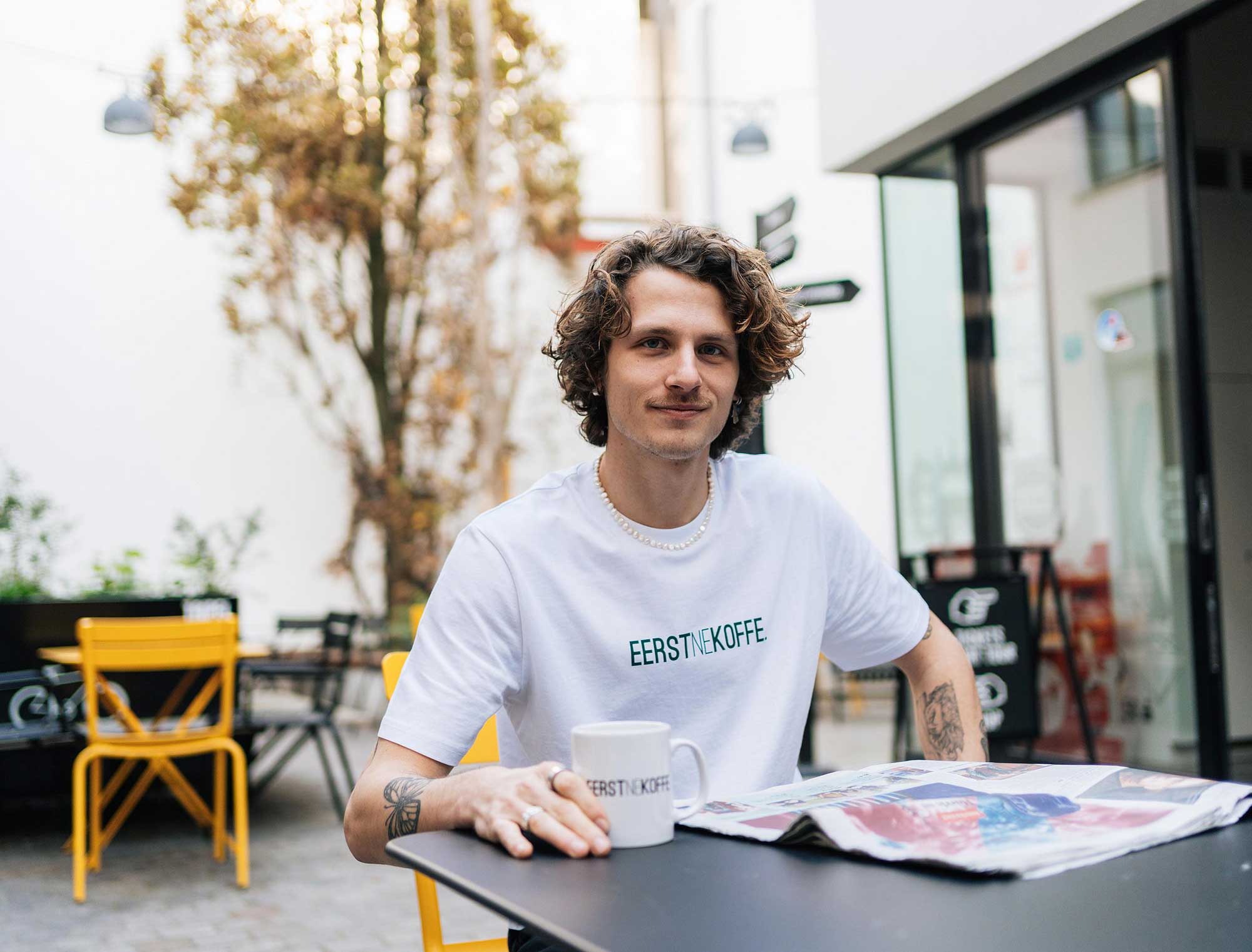 Man met een witte T-shirt met opdruk EERSTNEKOFFE. in 't groen.