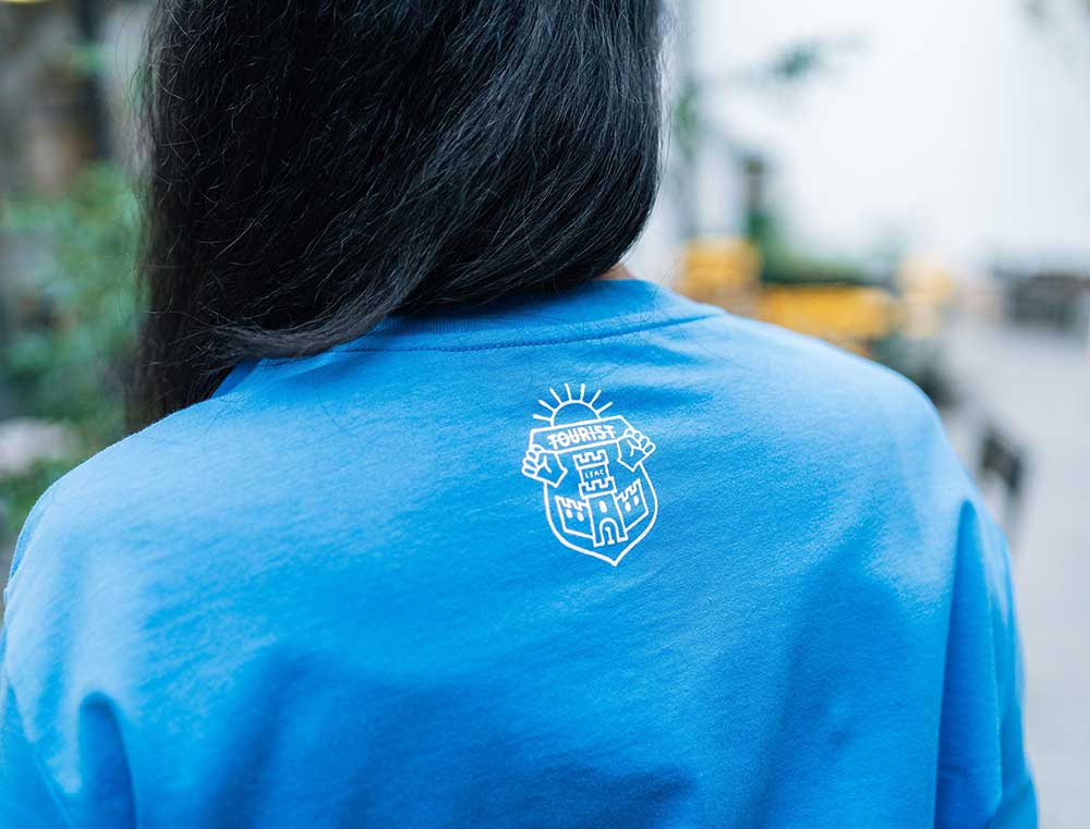 Achterkant van een blauwe T-shirt met het wapenschild van Tourist LeMC.