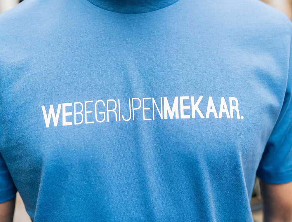Close-up van een blauwe T-shirt met opdruk WEBEGRIJPENMEKAAR.