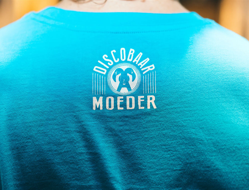 Close-up van logo Discobaar A Moeder op achterkant van blauwe T-shirt 