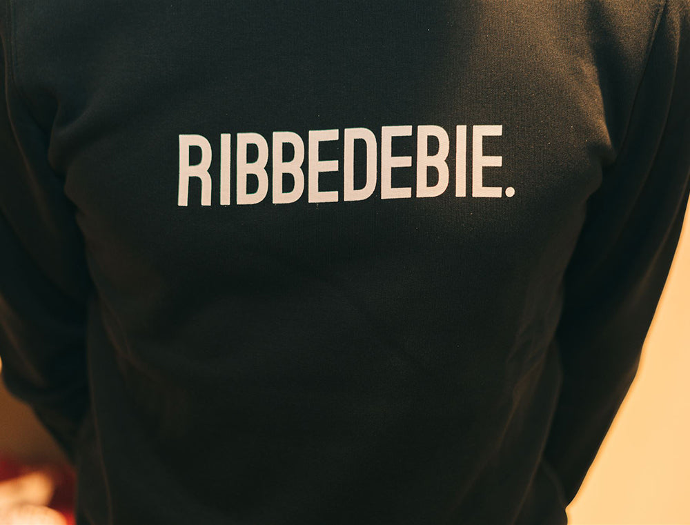 Close-up van zwarte sweater met opdruk RIBBEDEBIE.