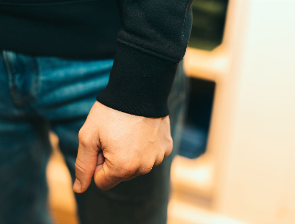 Close-up van pasvorm aan de hand van zwarte sweater met opdruk RIBBEDEBIE.