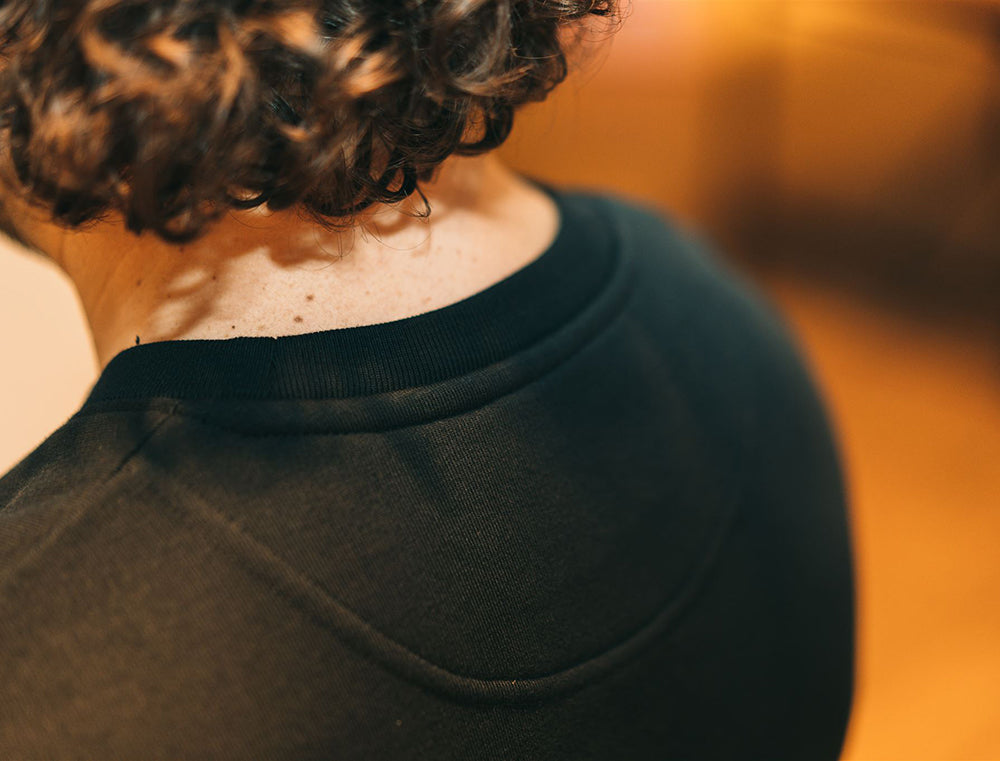 Close-up van pasvorm aan de nek van zwarte sweater met opdruk RIBBEDEBIE.