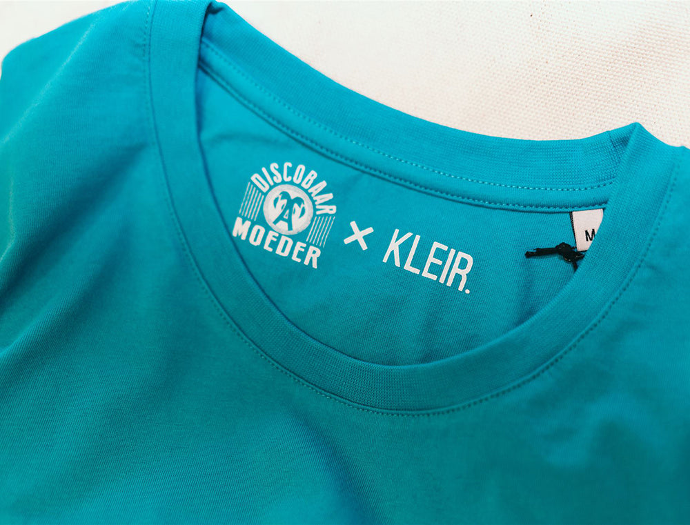 Close-up van logo's Discobaar A moeder x KLEIR. in een blauwe T-shirt