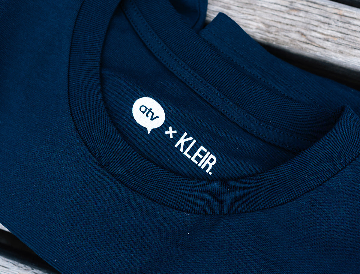 Close-up van een donkerblauwe T-shirt met de logo's van ATV en KLEIR.