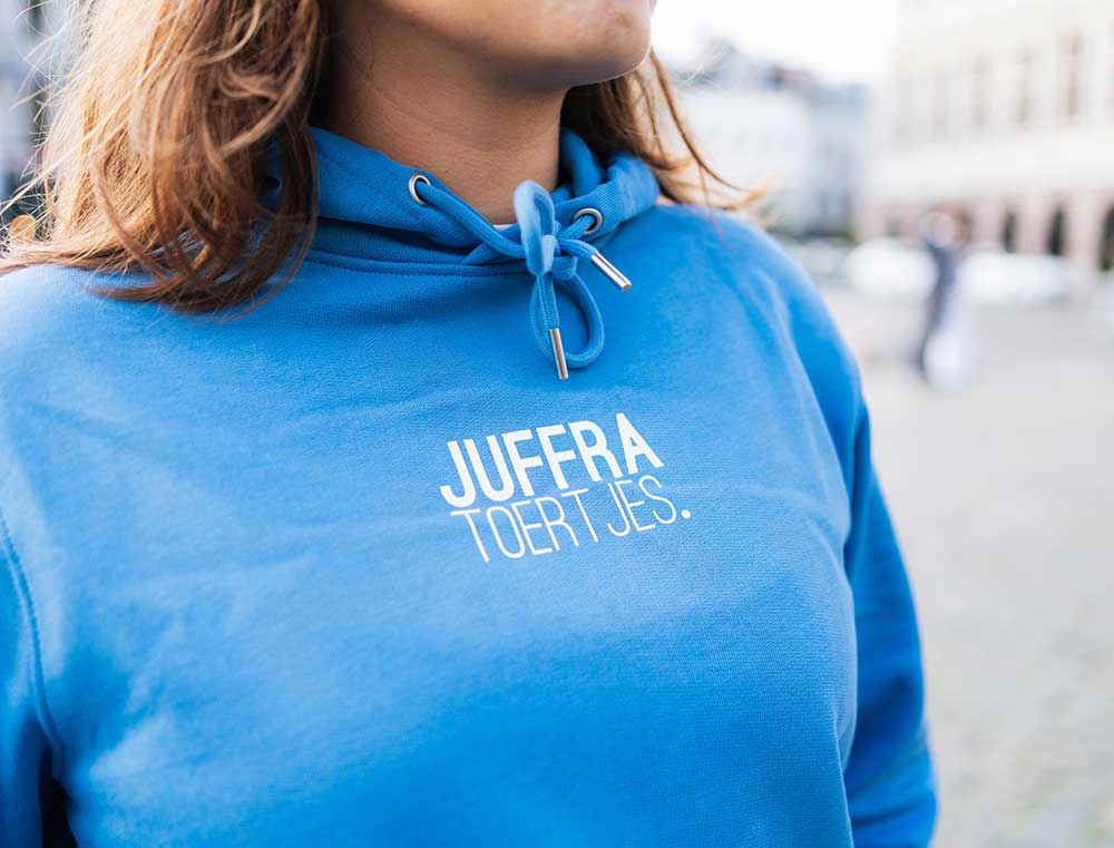 Vrouw met een lichtblauwe hoodie met opdruk 'JUFFRATOERTJES.'