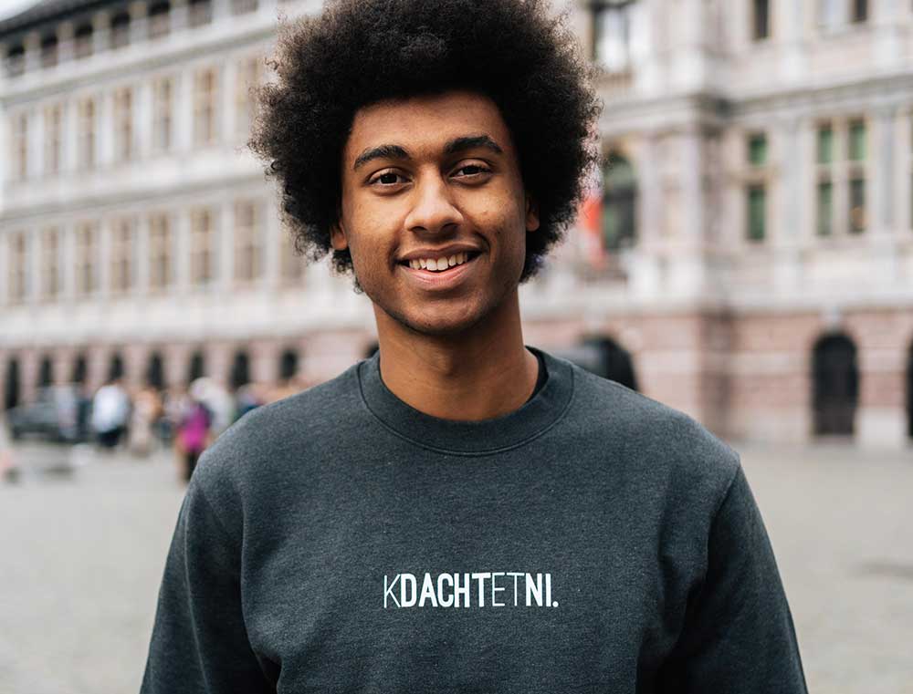 Man met een donkergrijze sweater met opdruk KDACHTETNI.