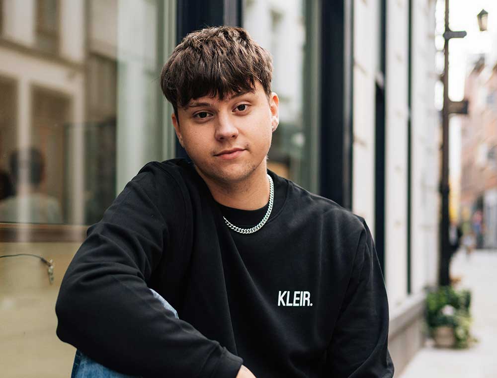 Man met een zwarte sweater met opdruk KLEIR. 