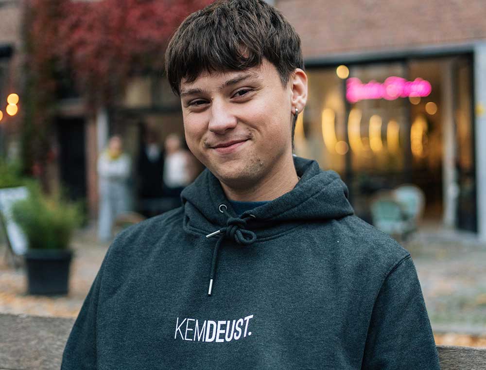 Man met een donkergrijze hoodie met opdruk KEMDEUST.