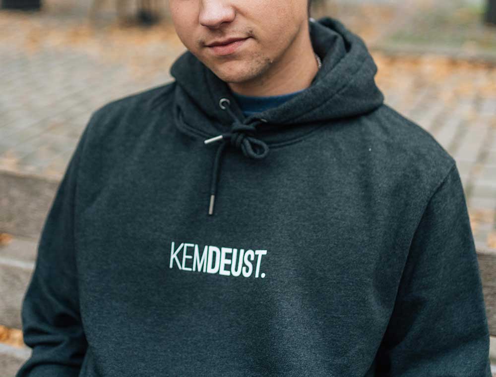 Man met een donkergrijze hoodie met opdruk KEMDEUST.