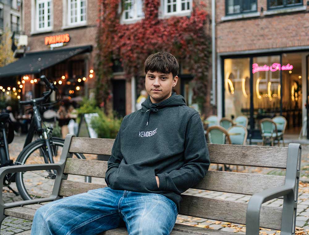 Man met een grijze hoodie met opdruk KEMDEUST.