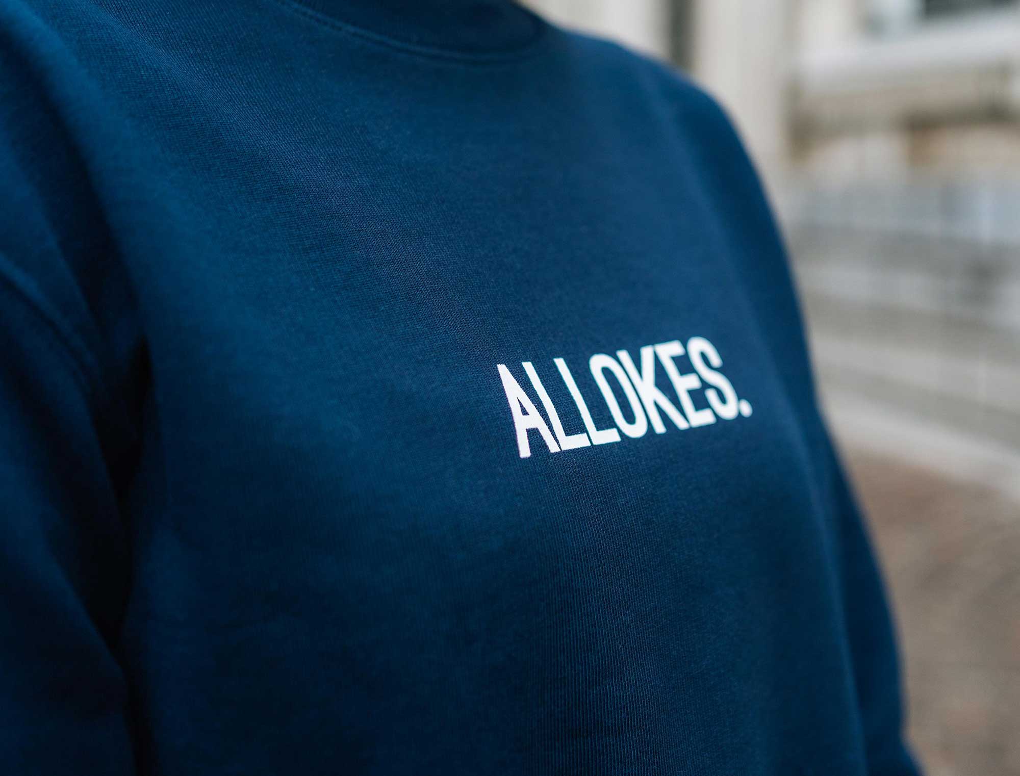 Close-up van een donkerblauwe sweater met opdruk ALLOKES.