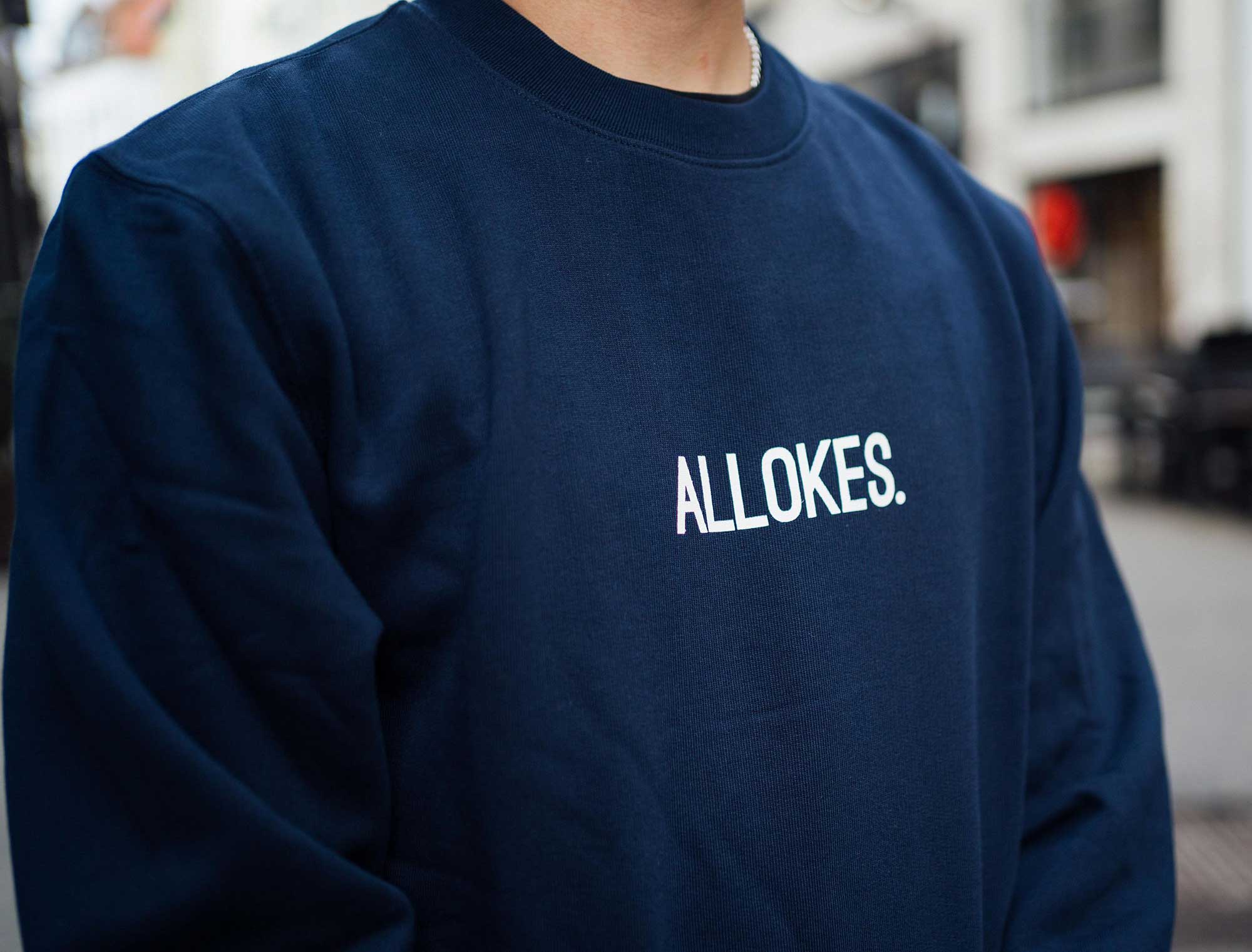 Close-up van een donkerblauwe sweater met opdruk ALLOKES.