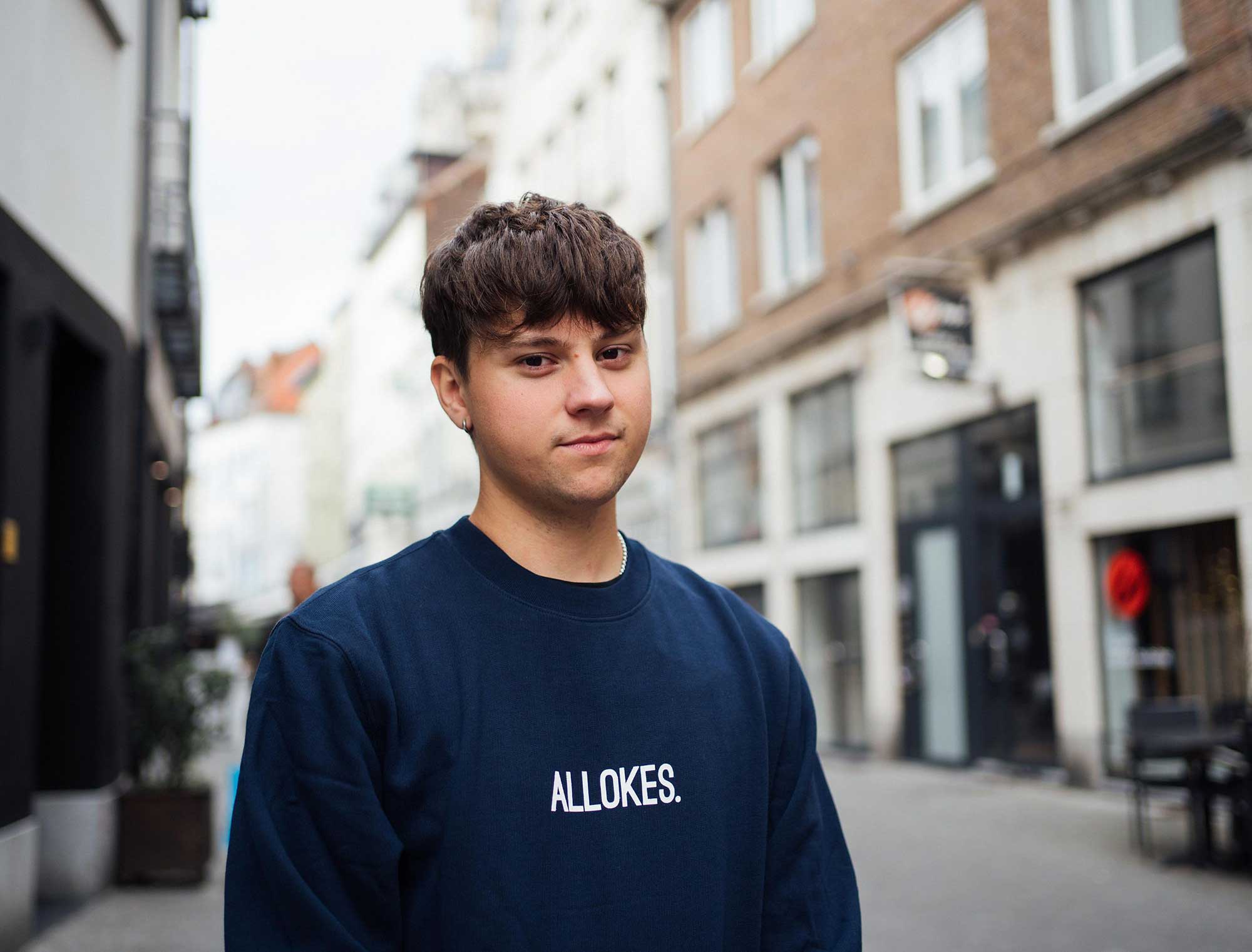Man met een donkerblauwe sweater met opdruk ALLOKES.