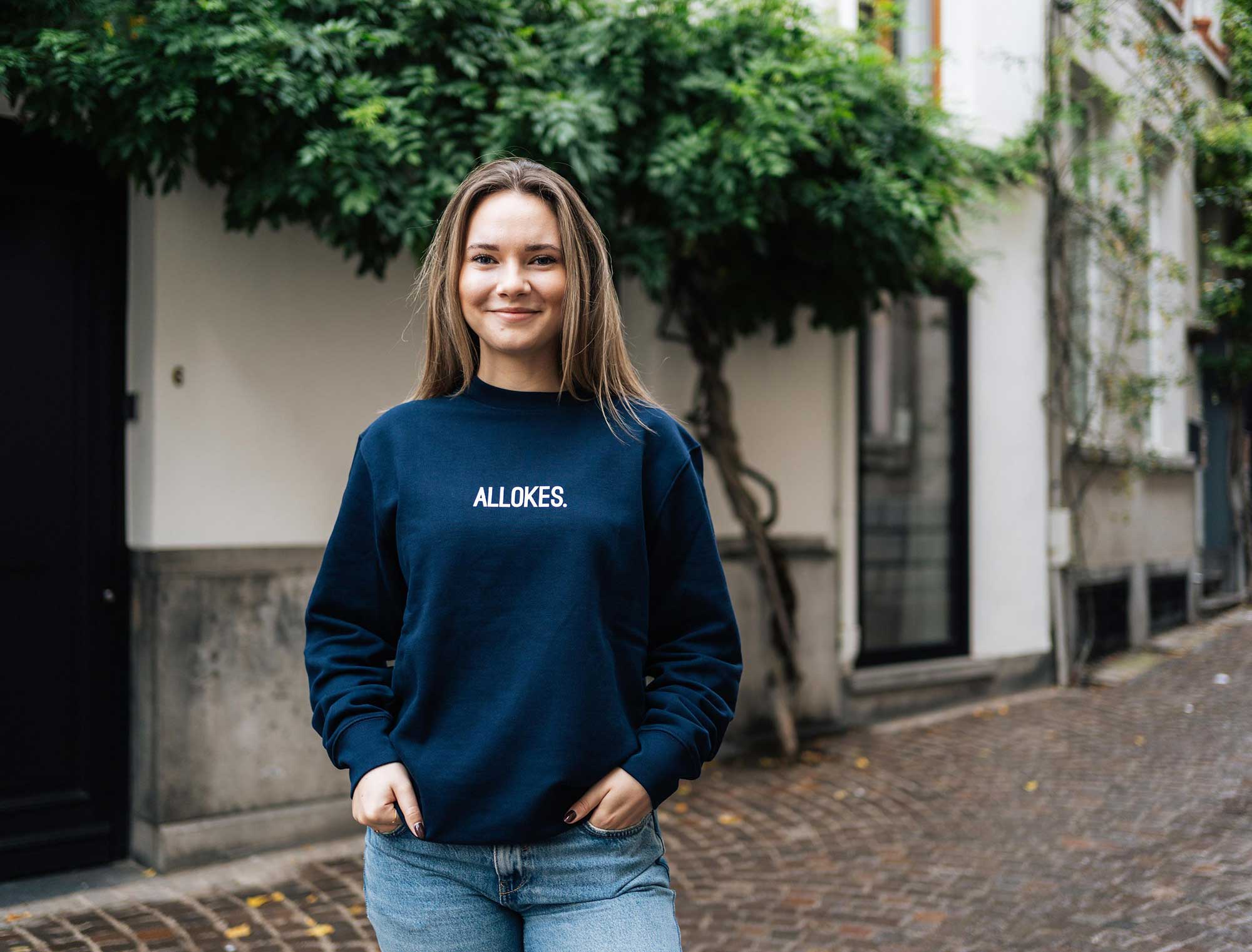 Vrouw met een donkerblauwe sweater met opdruk ALLOKES.