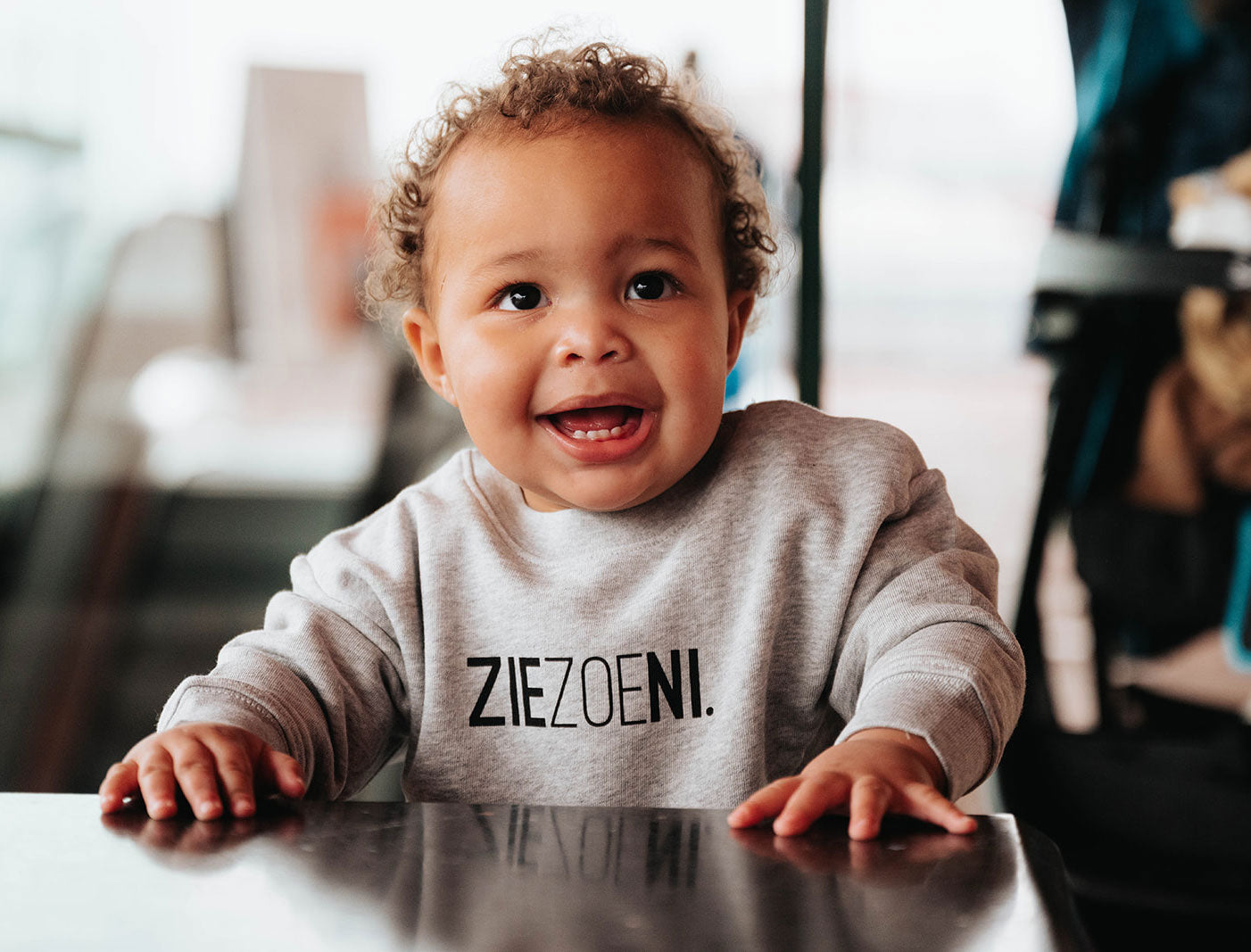 Baby met een grijze trui voor baby's met opdruk ZIEZOENI.