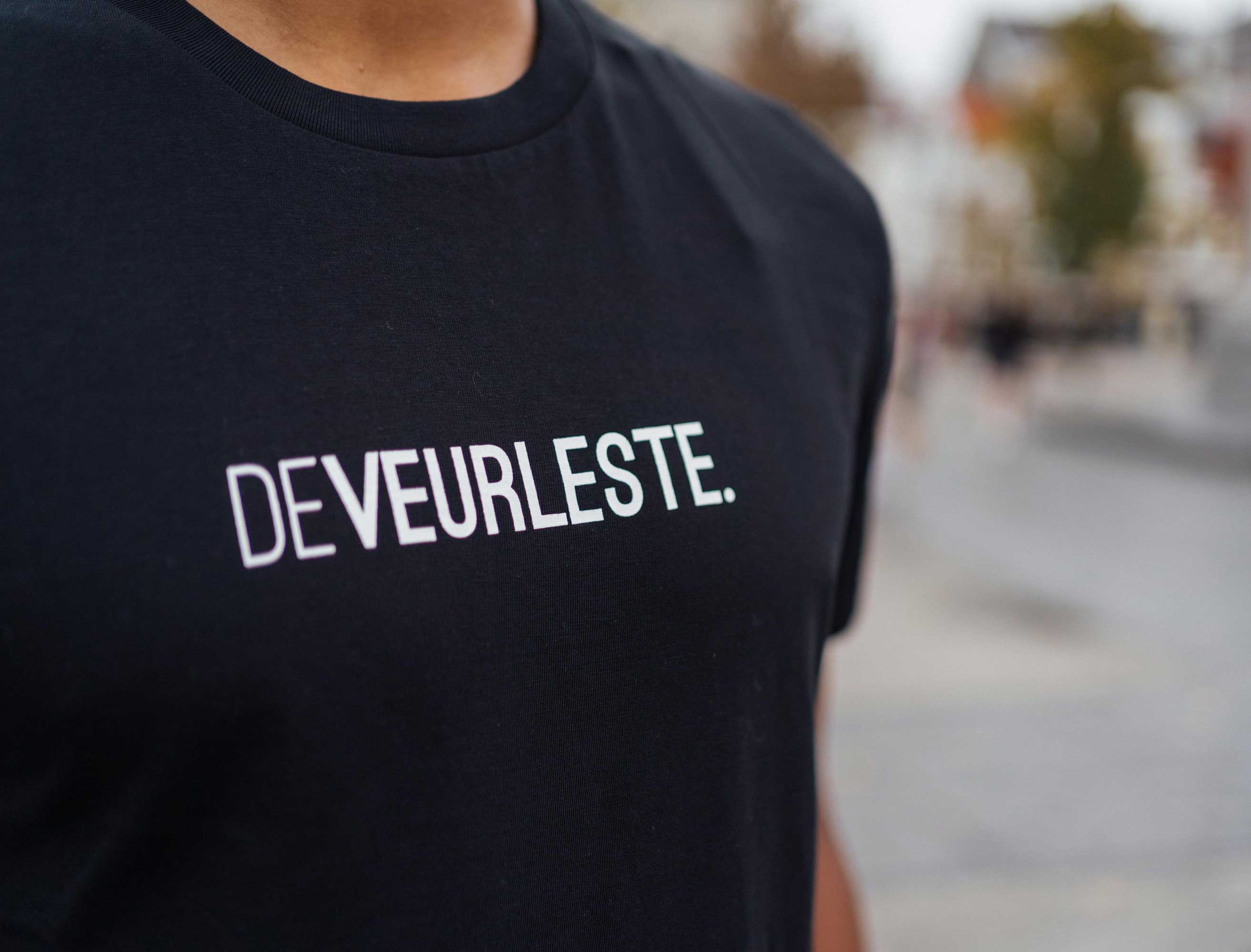 Close-up van een zwarte T-shirt met opdruk DEVEURLESTE.