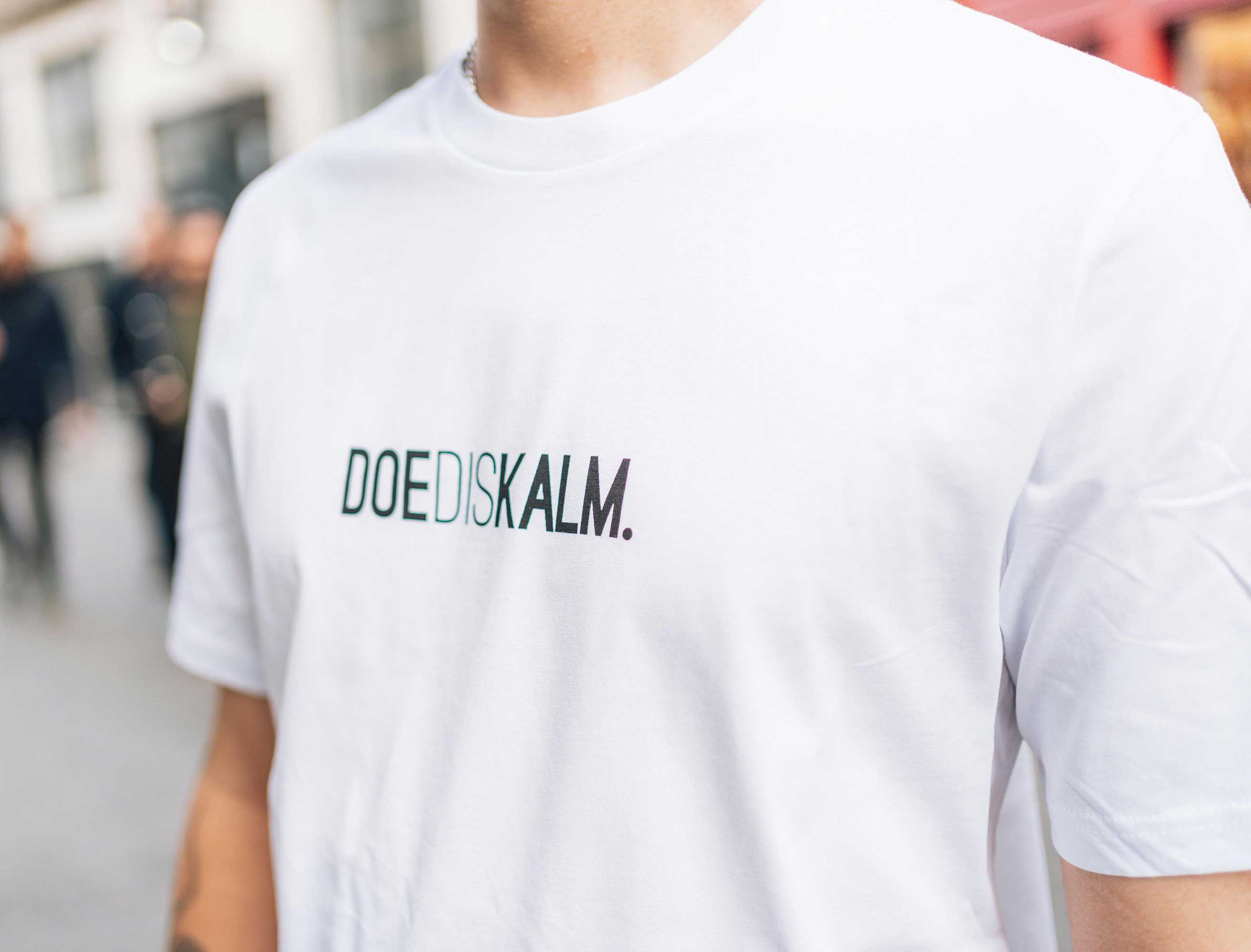 Close-up van een witte T-shirt met opdruk DOEDISKALM.
