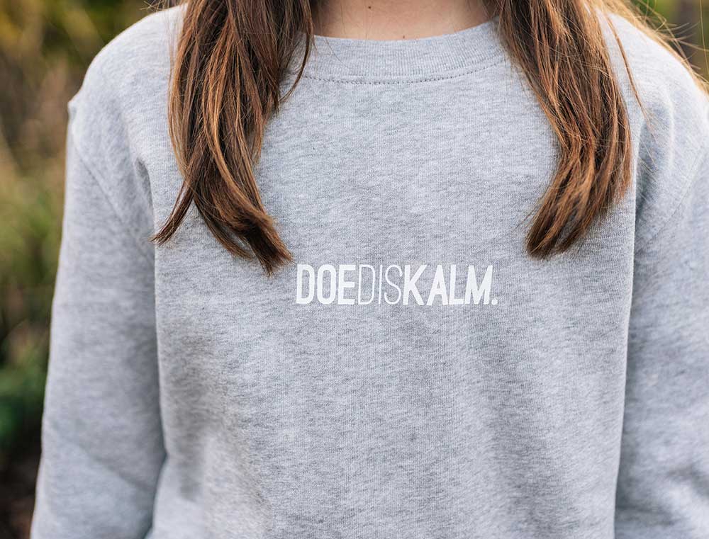 Close-up van een grijze sweater met opdruk DOEDISKALM. voor kinderen