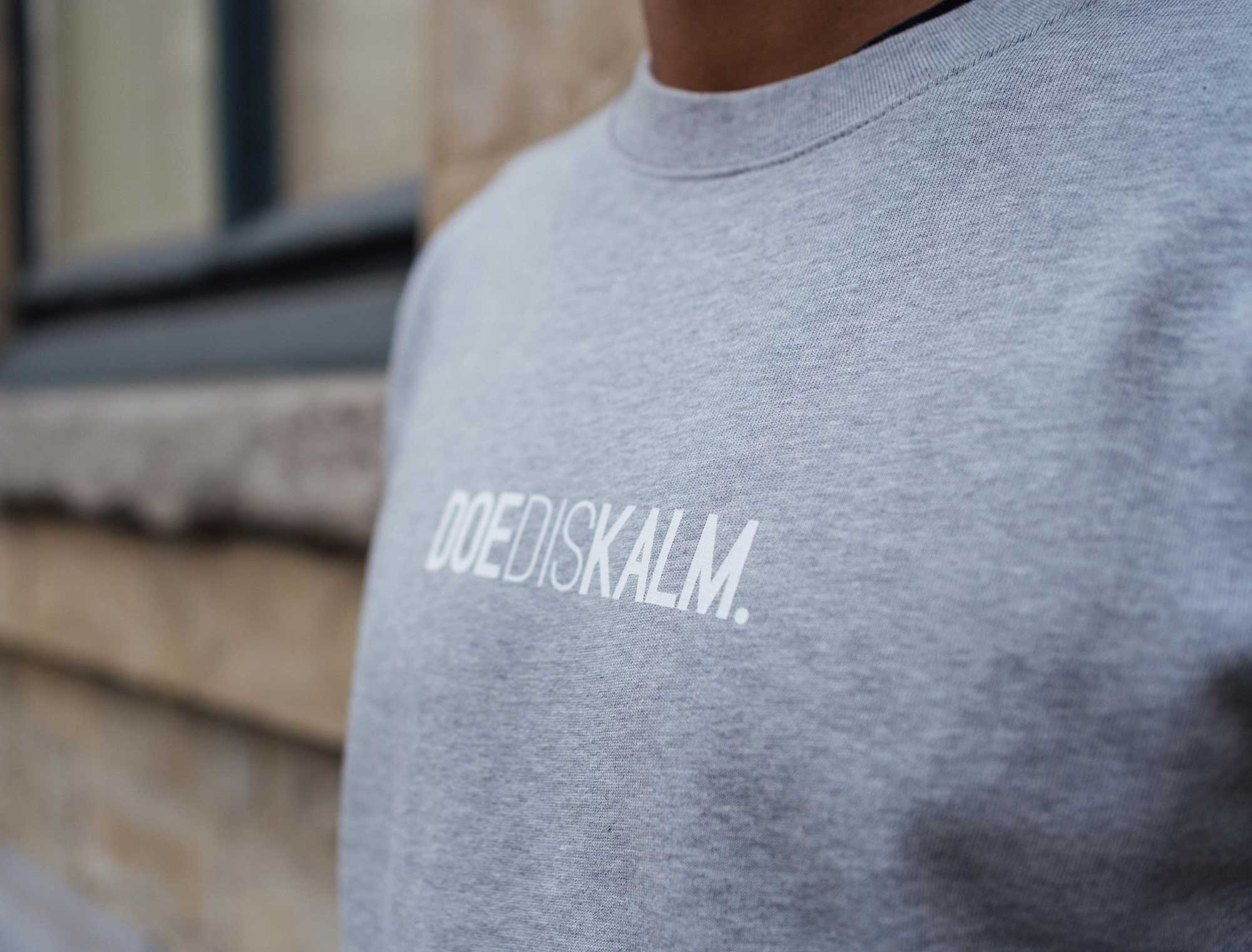 Close-up van een grijze sweater met opdruk DOEDISKALM.