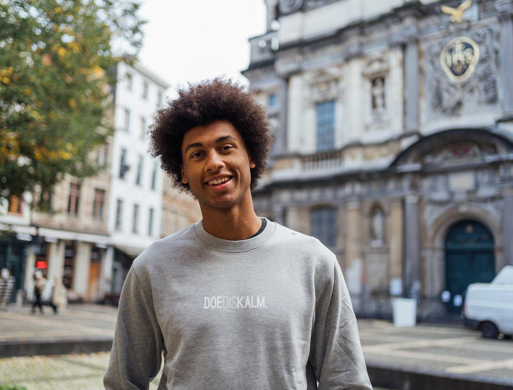 Man met een grijze sweater met opdruk DOEDISKALM.