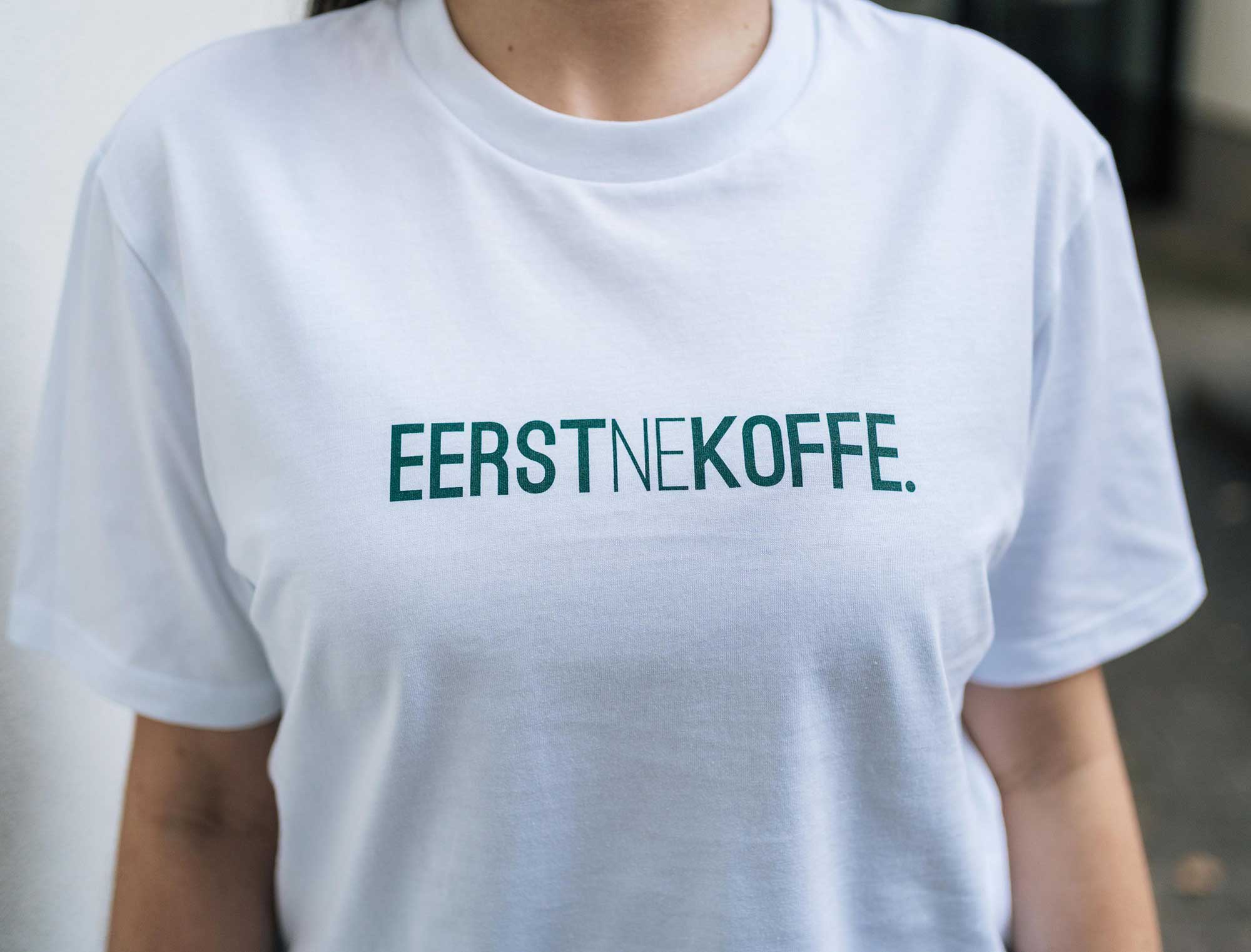 Detail van een witte T-shirt met opdruk EERSTNEKOFFE. 