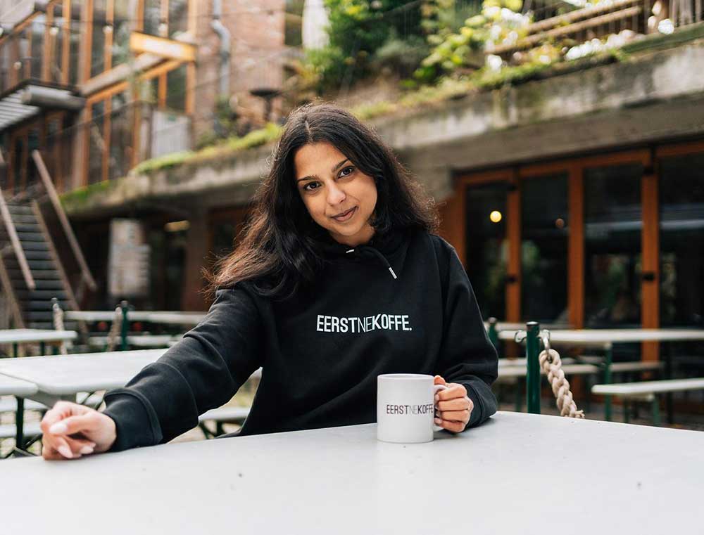 Vrouw met een zwarte hoodie met opdruk EERSTNEKOFFE.
