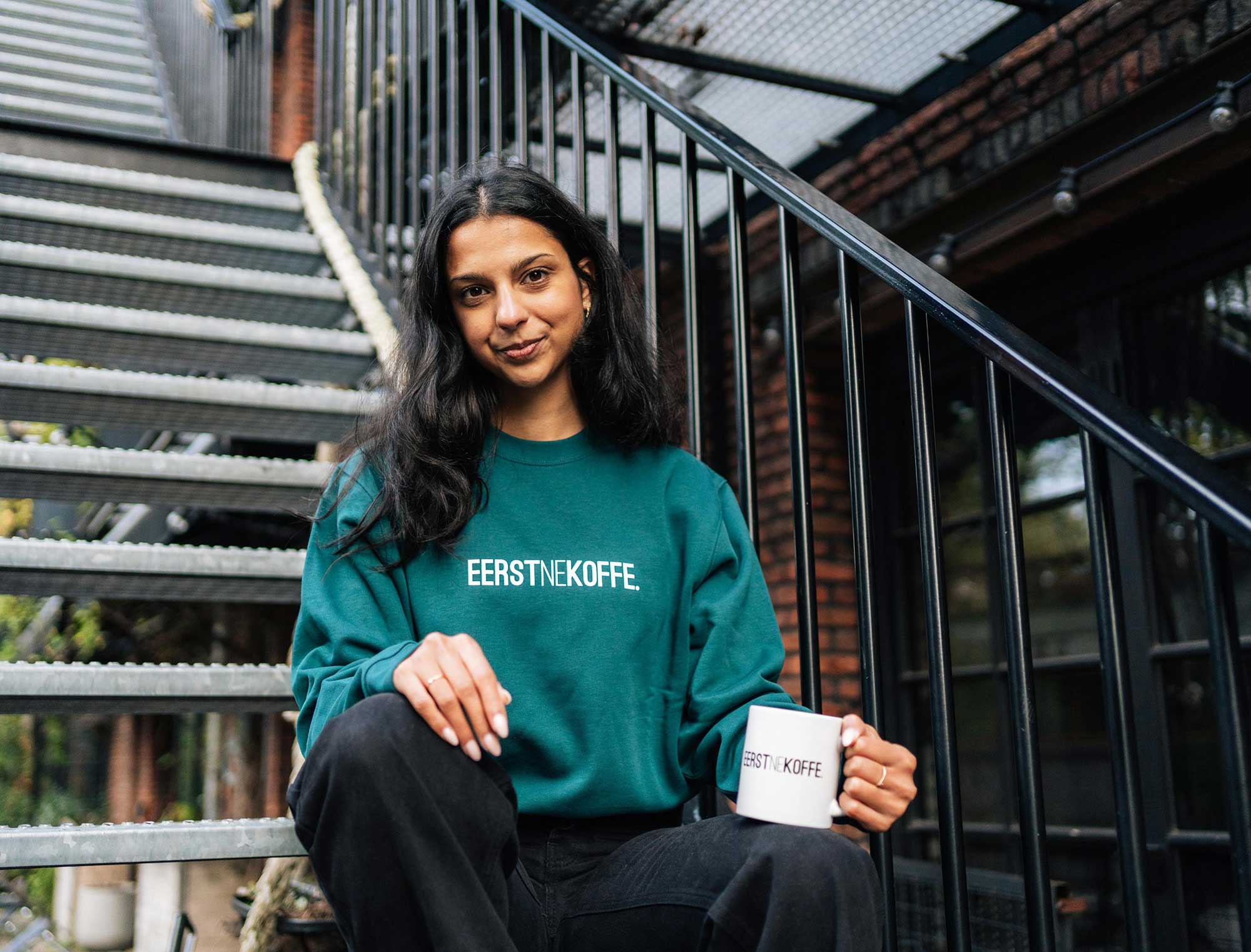 Vrouw met een groene sweater met opdruk EERSTNEKOFFE.