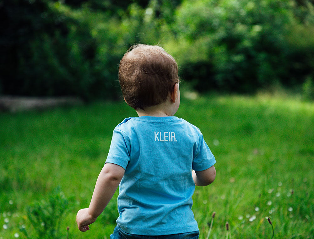 baby met blauwe T-shirt met opdruk KLEIR. op de achterkant 