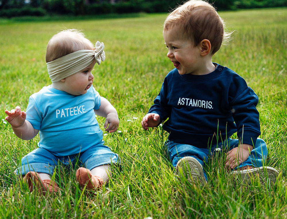 Baby met blauwe T-shirt met opdruk PATEEKE. Baby met donkerblauwe sweater met opdruk ASTAMORIS.