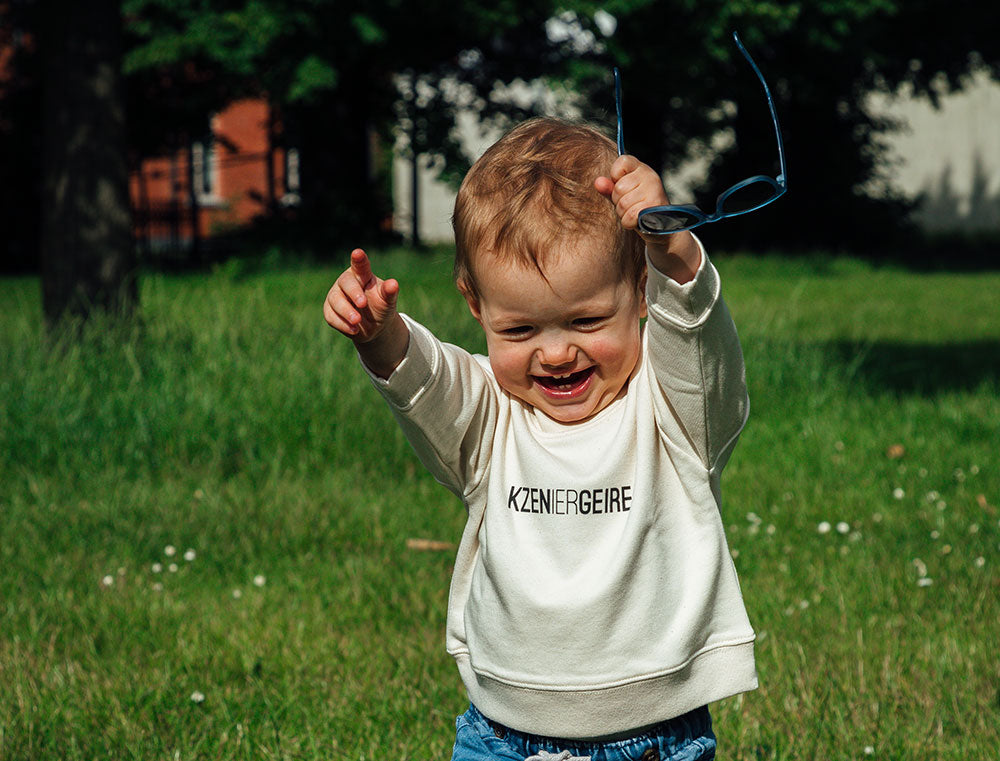 Baby met witte sweater met opdruk KZENIERGEIRE.
