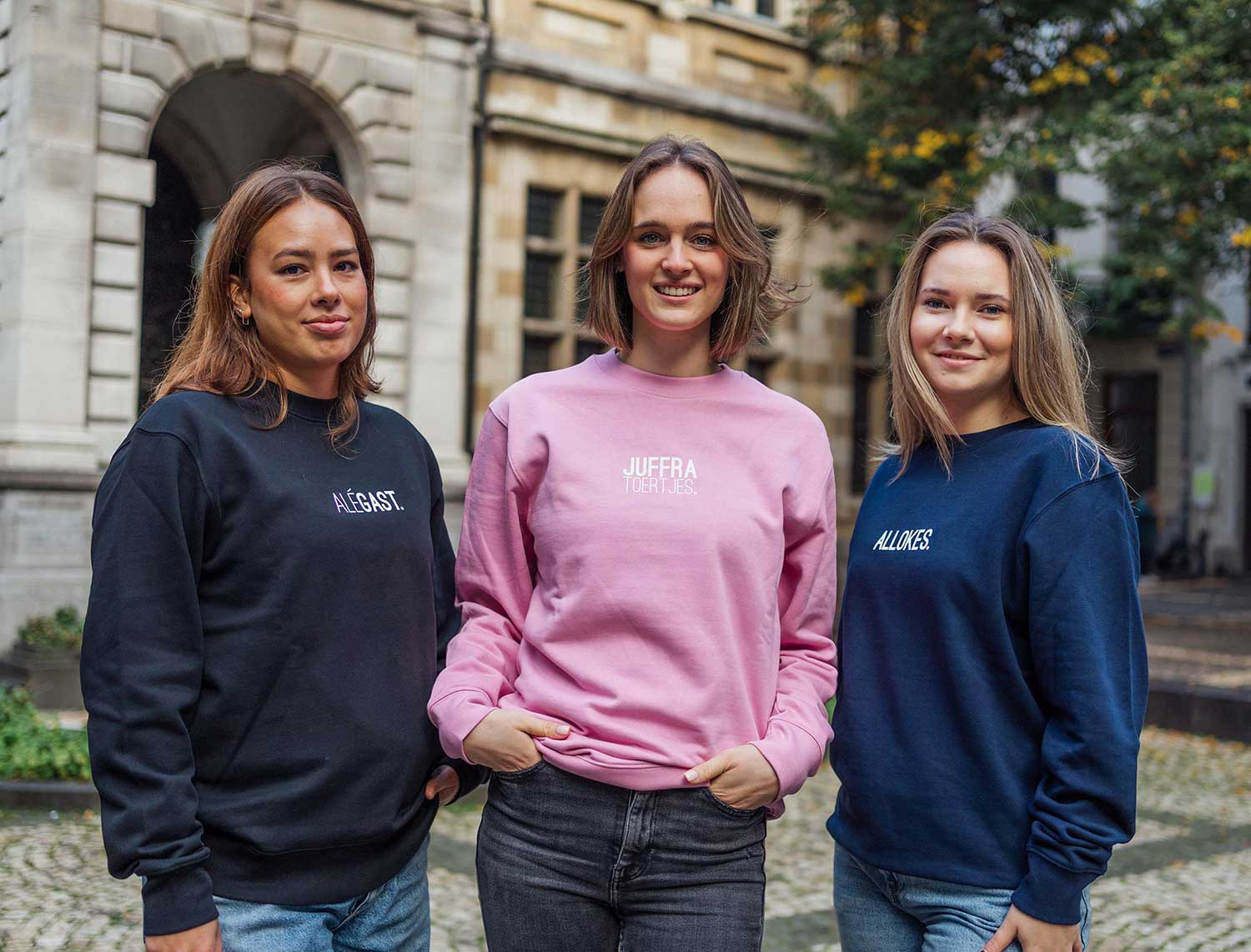 3 vrouwen met kledij van KLEIR. De middelste draagt een roze sweater met opdruk JUFFRA TOERTJES.