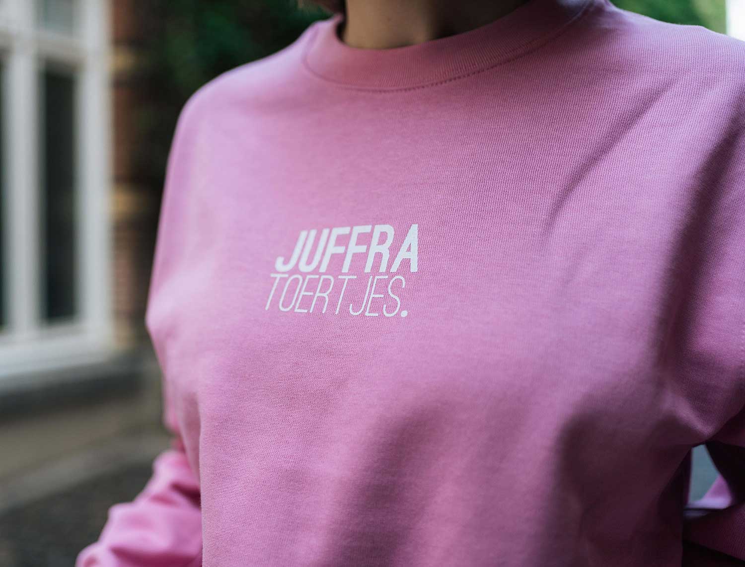 Close-up van een roze sweater met opdruk JUFFRA TOERTJES.