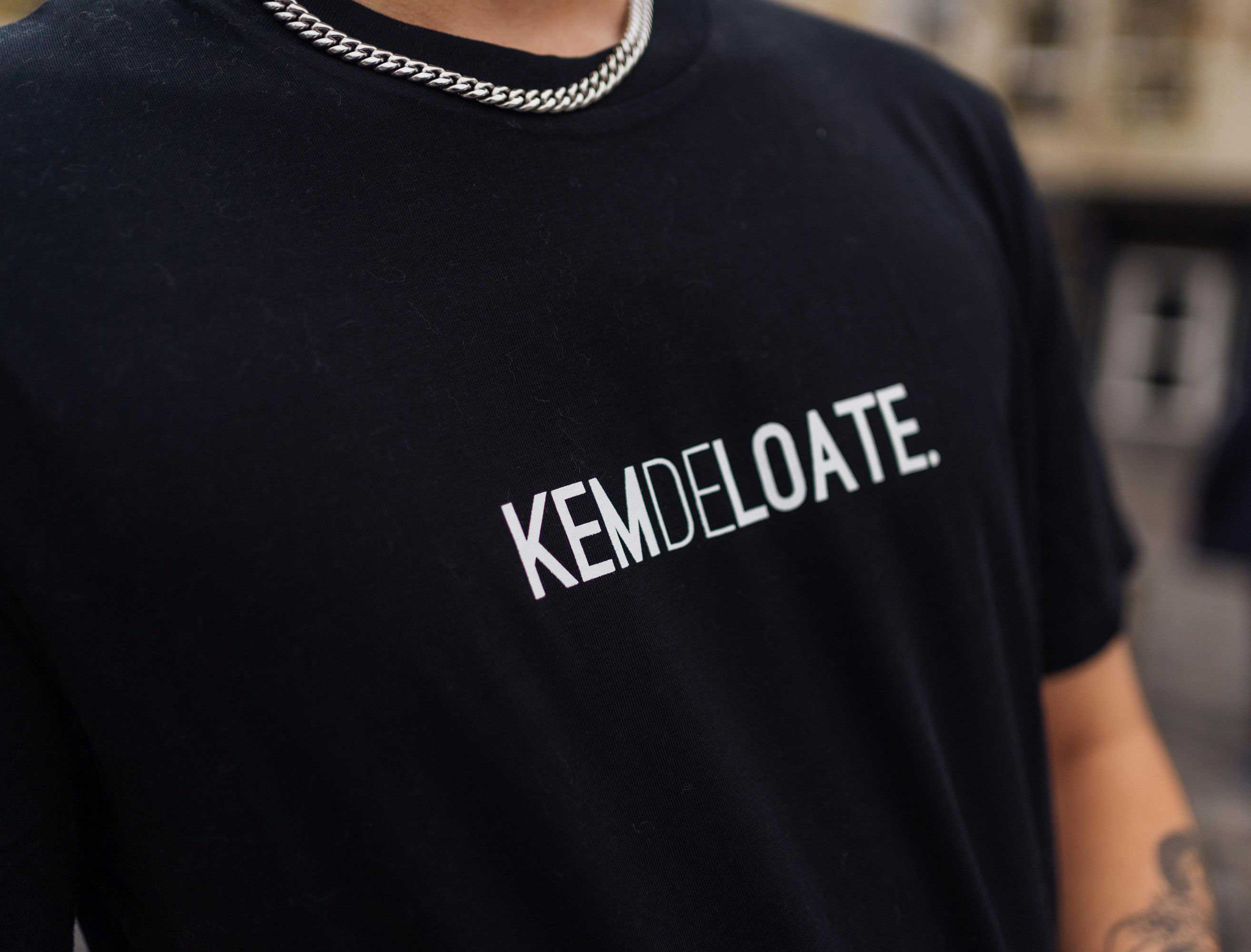 Close-up van een zwarte T-shirt met opdruk KEMDELOATE.
