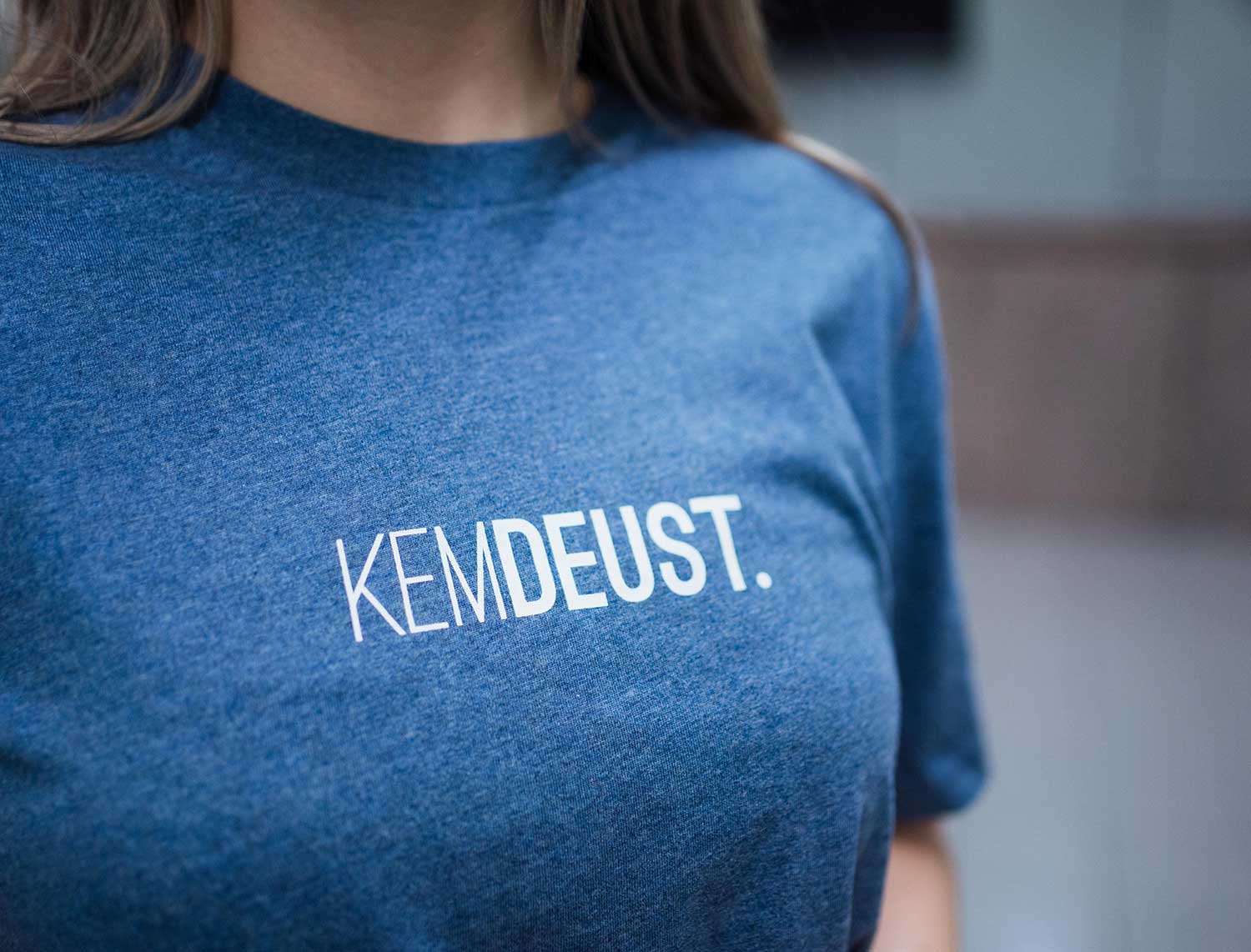 Close-up van een blauwe T-shirt met opdruk KEMDEUST.