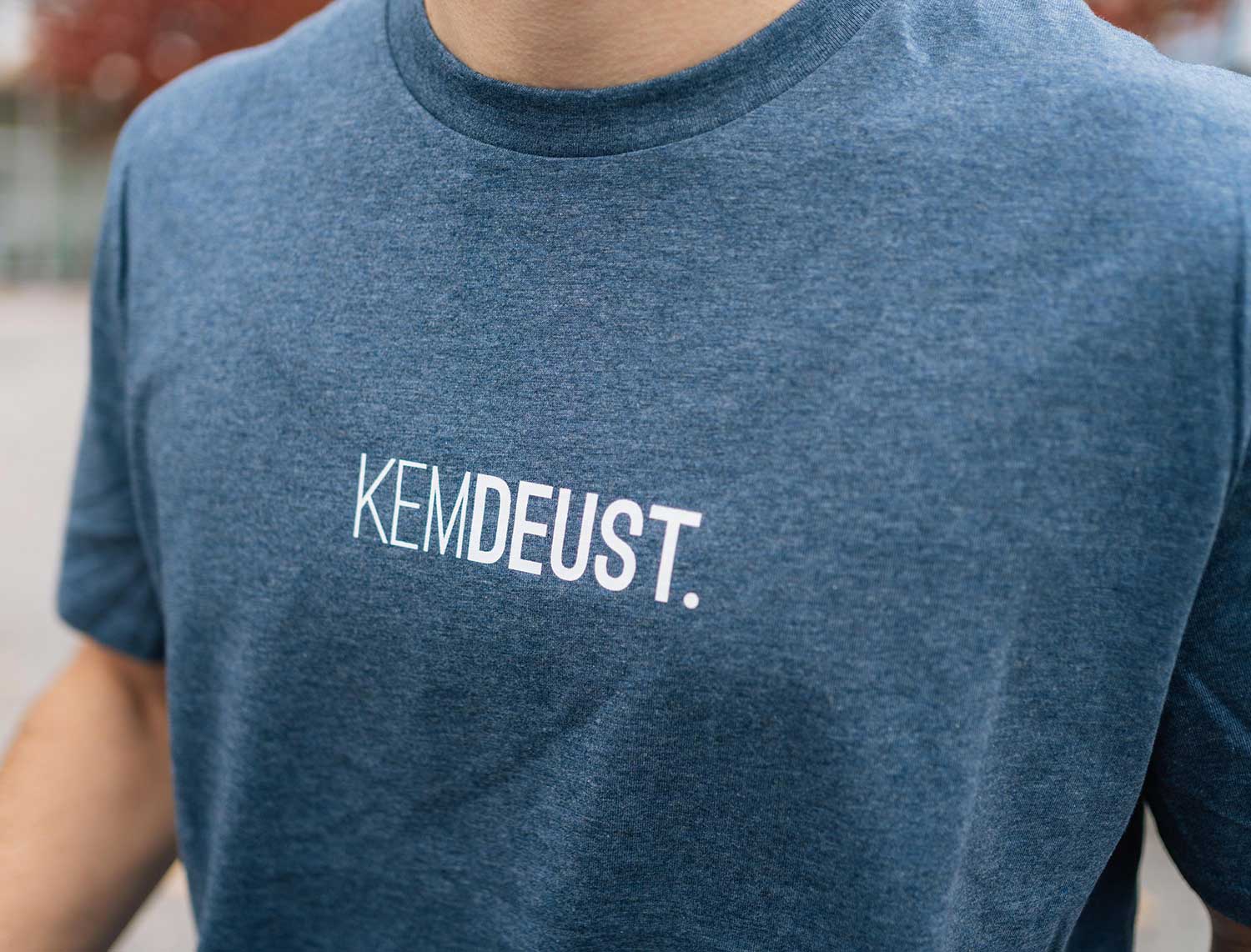 Close-up van een blauwe T-shirt met opdruk KEMDEUST.