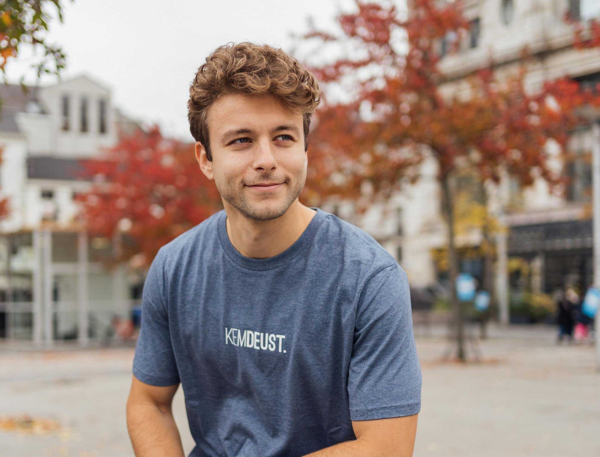 Man met een blauwe T-shirt met opdruk KEMDEUST.