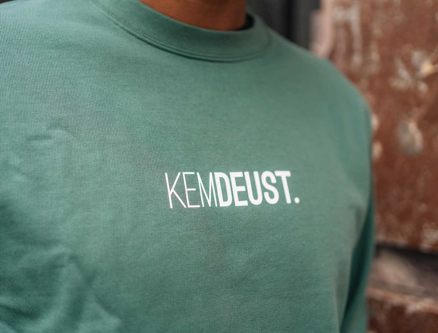 Close-up van een groene sweater met opdruk KEMDEUST.