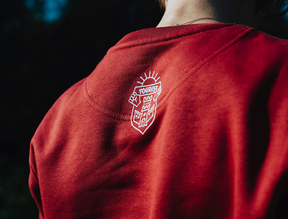Close-up van logo TOURIST op achterkant van rode sweater