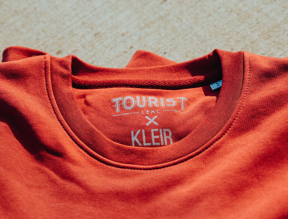 Close-up van rode T-shirt nek met logo TOURIST en KLEIR.