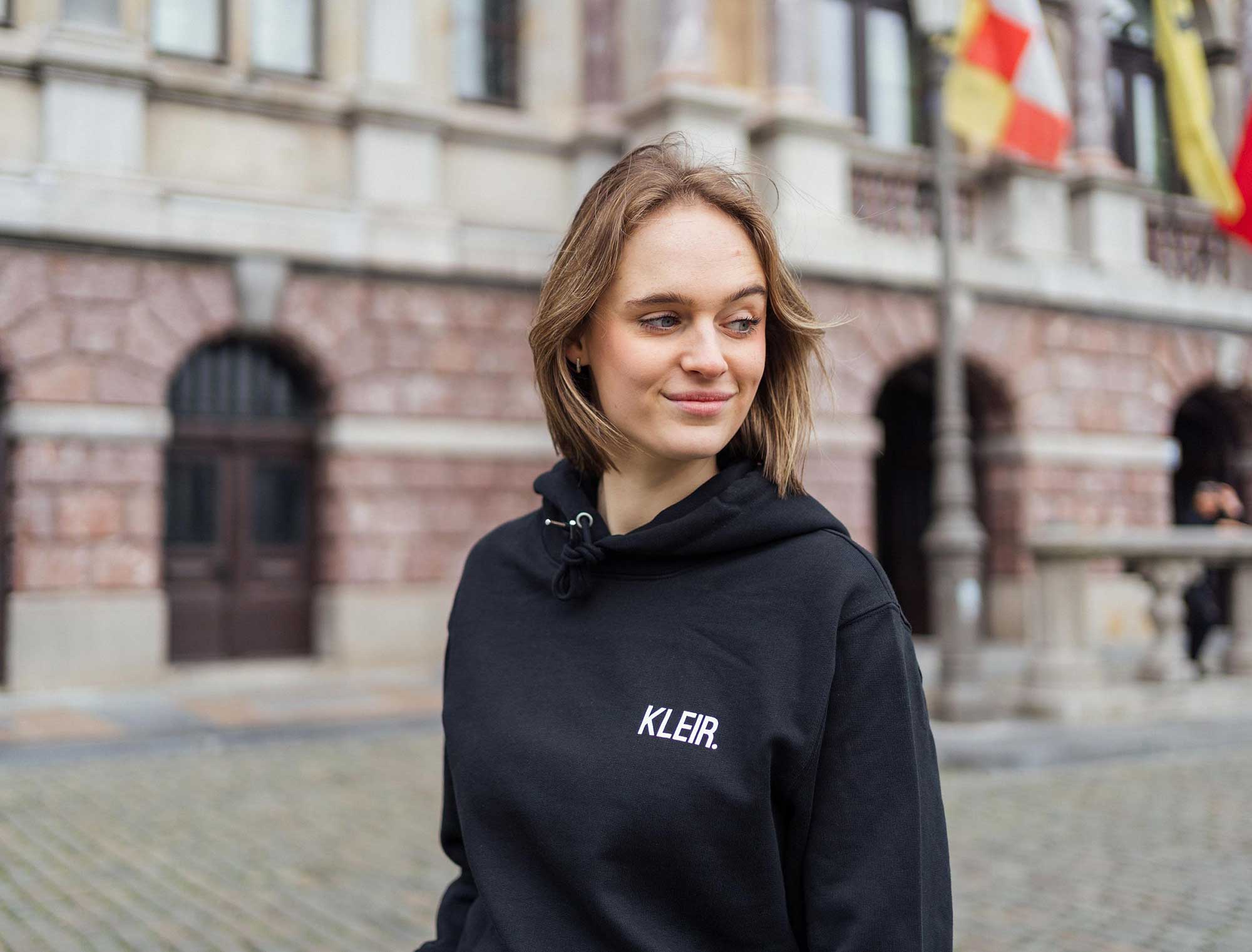 Vrouw met een zwarte hoodie met opdruk KLEIR.