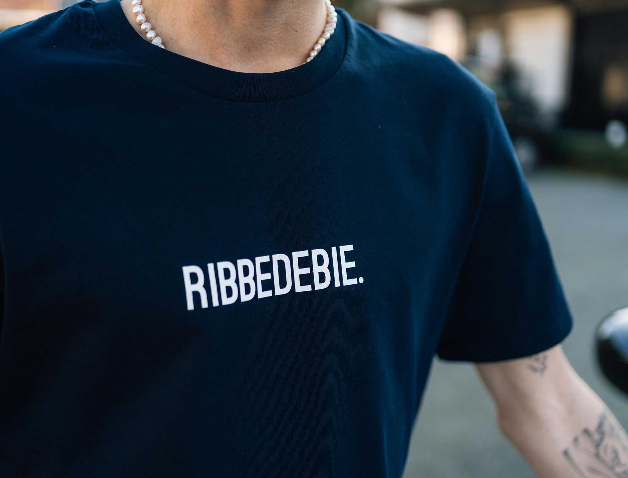 Close-up van een donkerblauwe T-shirt met opdruk RIBBEDEBIE.