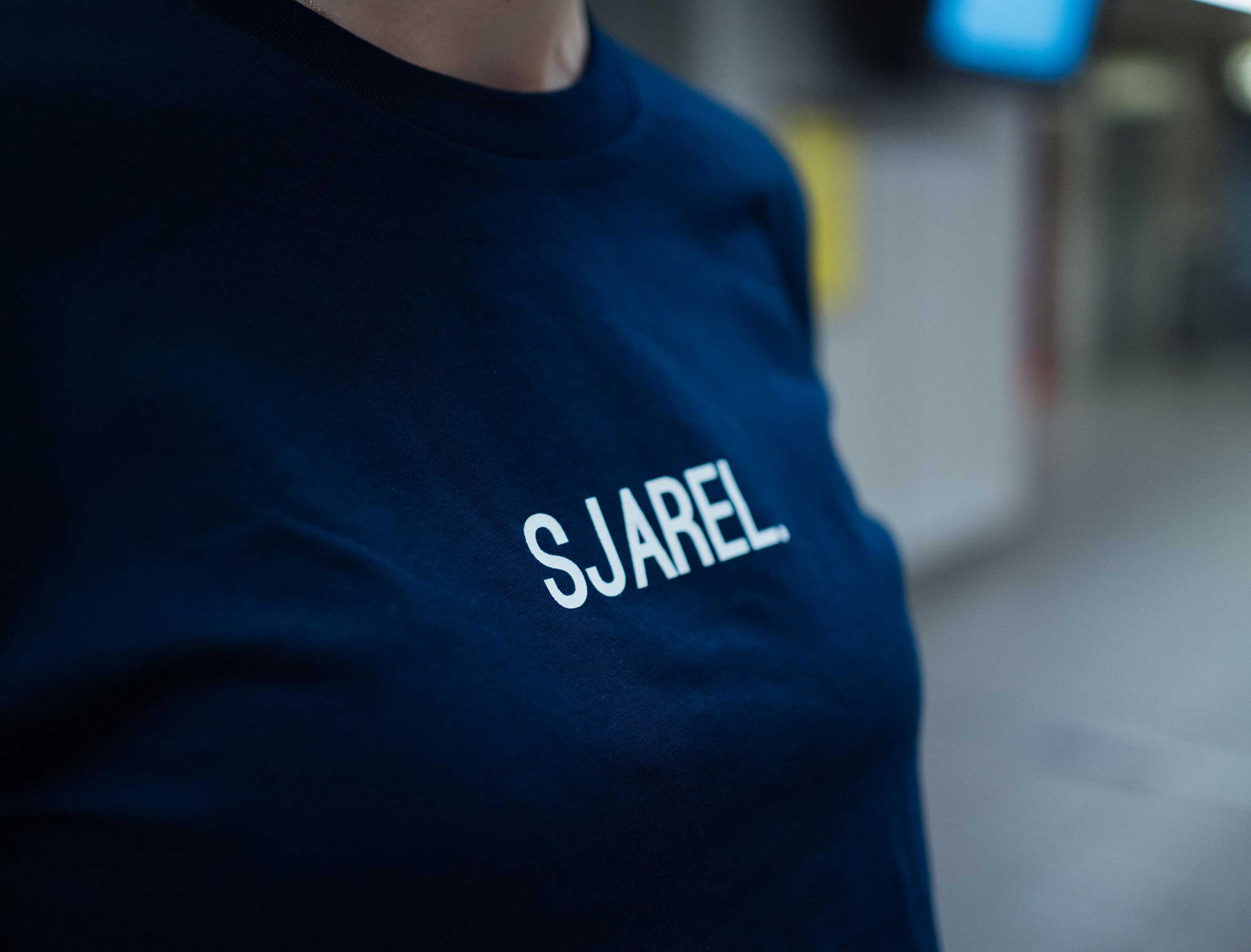 Close-up van een donkerblauwe T-shirt met opdruk SJAREL.