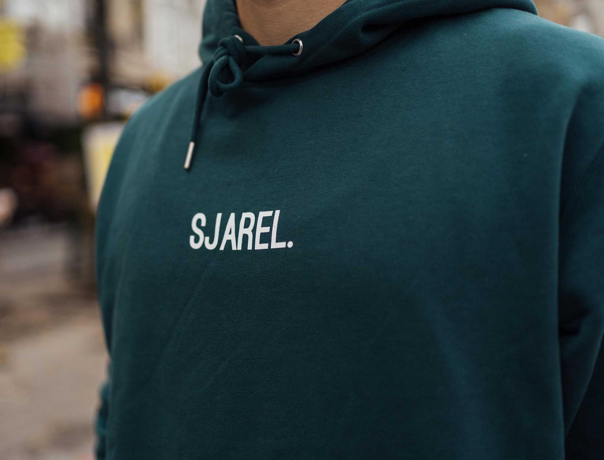 Close-up van een groene hoodie met opdruk SJAREL.