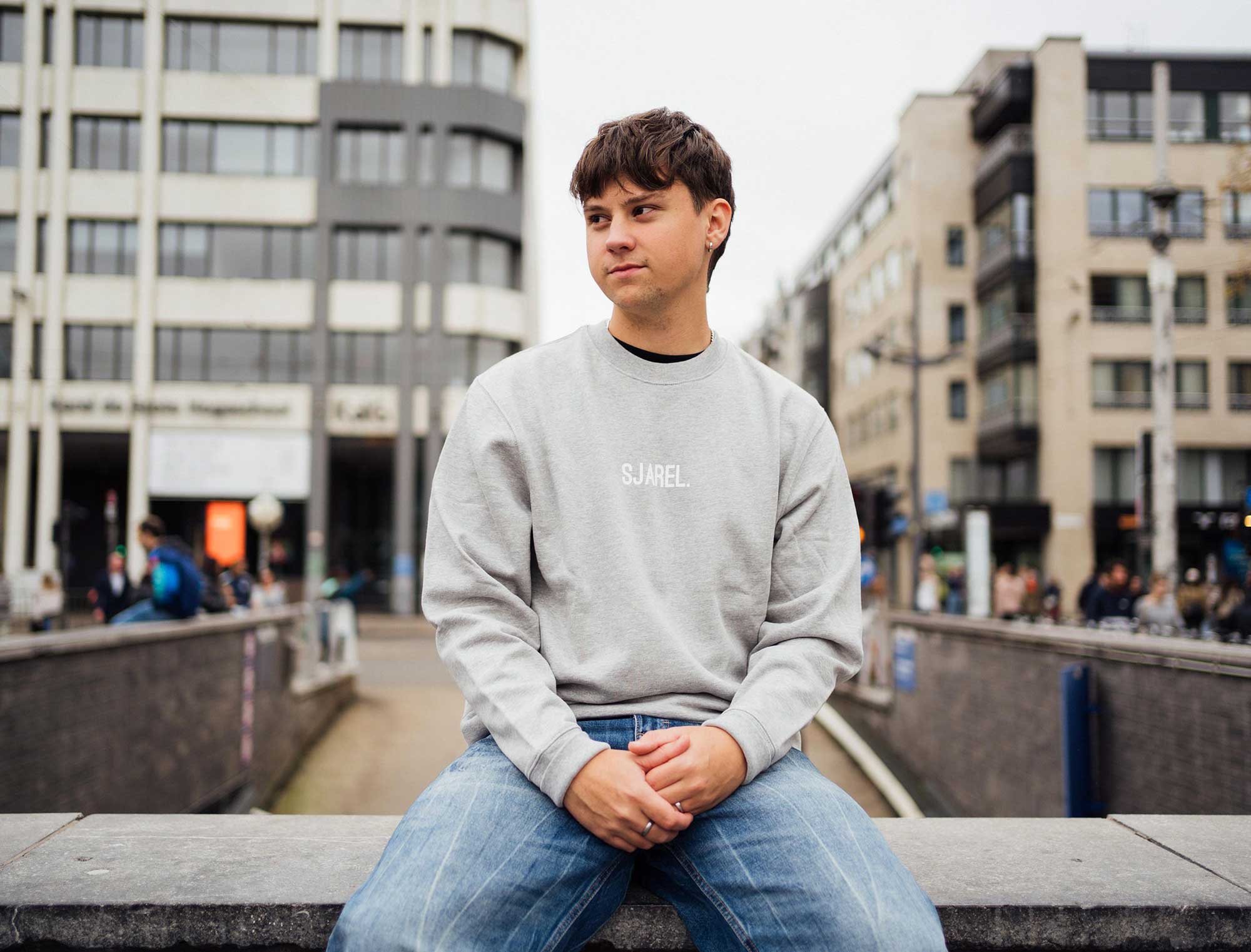 Man met een grijze sweater met opdruk SJAREL.