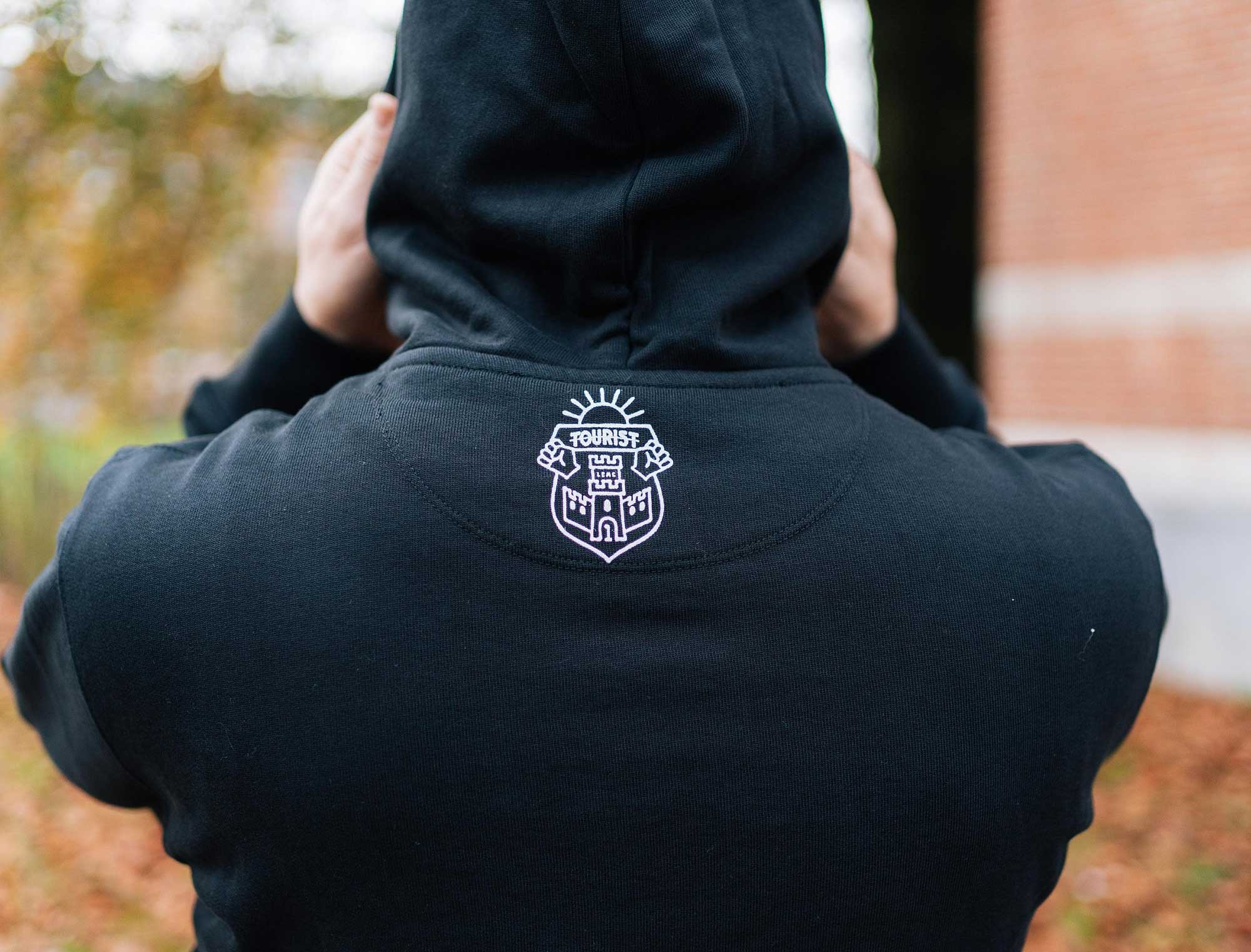 Achterkant van een zwarte hoodie met het wapenschild van Tourist LeMC