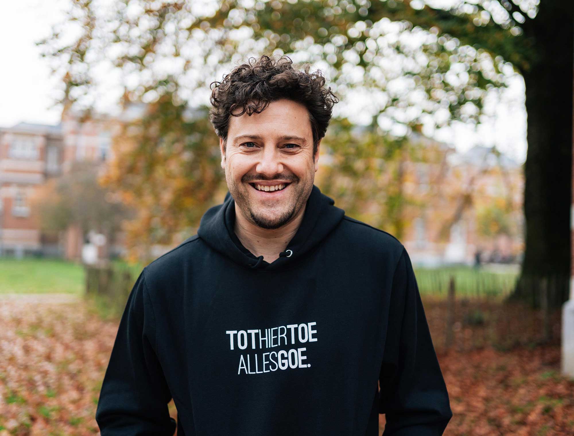Man met een zwarte hoodie met opdruk TOTHIERTOEALLESGOE.