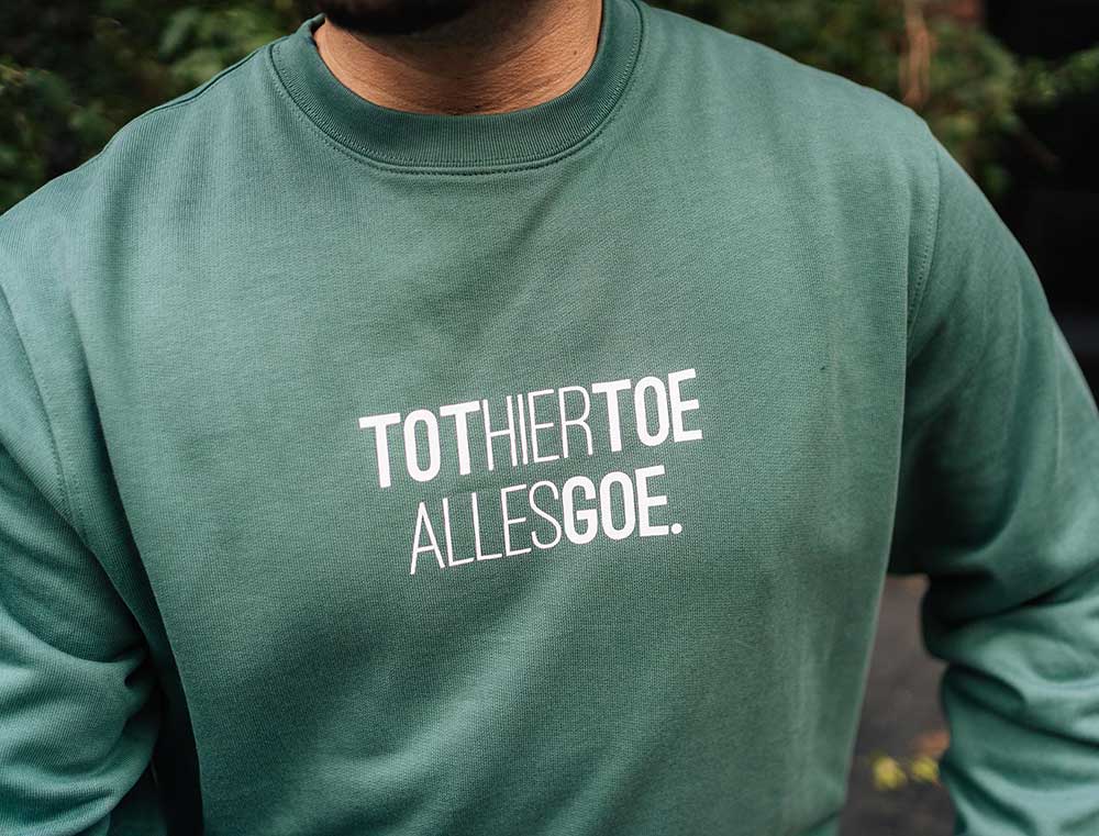 Close-up van een groene trui met opdruk TOTHIERTOEALLESGOE.