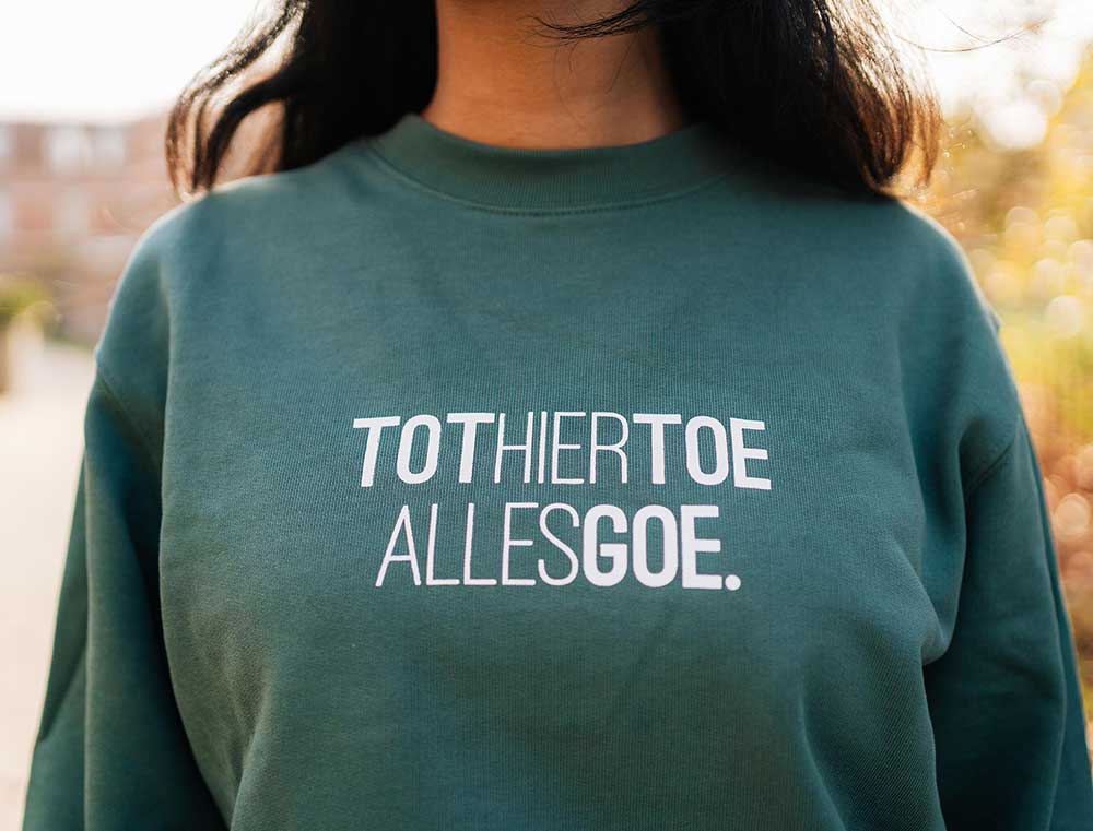 Close-up van een groene trui met opdruk TOTHIERTOEALLESGOE.