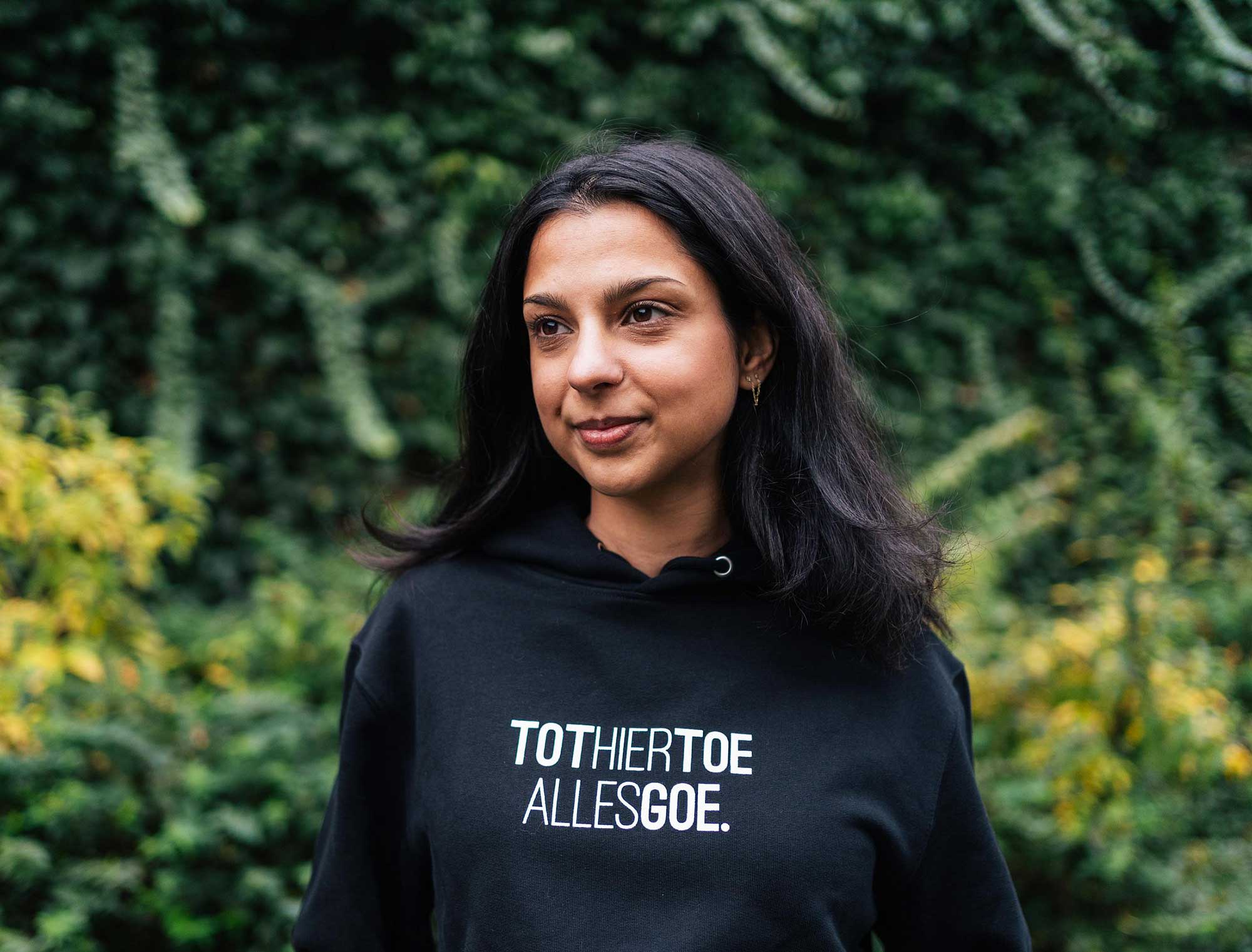 Vrouw met een zwarte hoodie met opdruk TOTHIERTOEALLESGOE.
